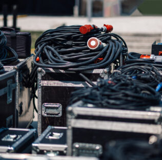 Neatly arranged black audio cables on metal cases outdoors, ready for a concert. The setup showcases attention to detail in the entertainment industry