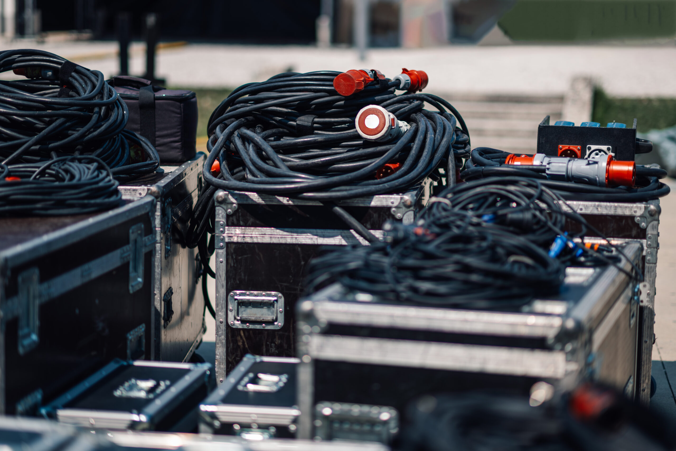 Neatly arranged black audio cables on metal cases outdoors, ready for a concert. The setup showcases attention to detail in the entertainment industry