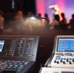 Live theater concert show sound video music control console with scene lights background. Sound engineer mixer soundboard equipment with many knobs, buttons, faders, equalizer screen and light.